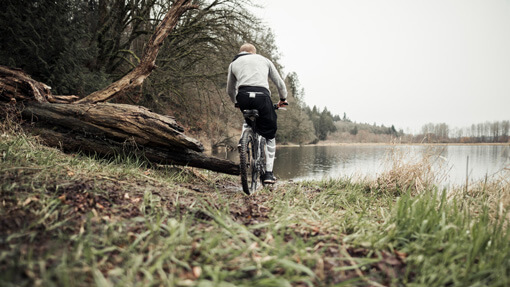 Fahrradfahrer faehrt am See bei grauem Wetter