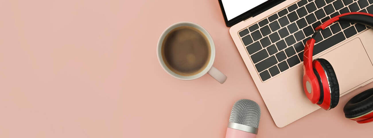 Kaffeetasse, Mikro, Laptop und Kopfhörer liegen auf rosa Untergrund, Vogelperspektive