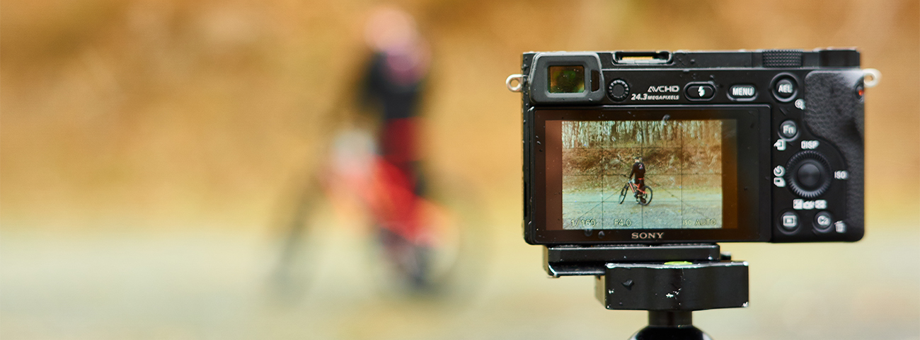 Eine Kamera im Vordergrund filmt einen fahrradfahrer, der verschwommen im Hintergrund steht