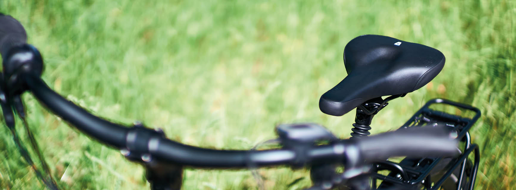 Ein Fahrradsattel und ein Lenker im Fokus. Im Hintergrund eine grüne Wiese
