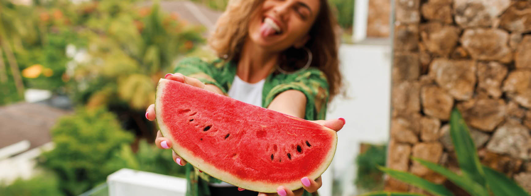 Eine Frau hält fröhlich ein Stück Wassermelone in die Kamera