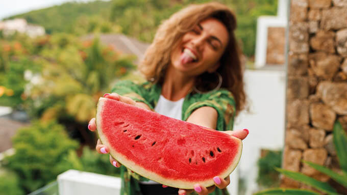 Eine Frau hält fröhlich ein Stück Wassermelone in die Kamera