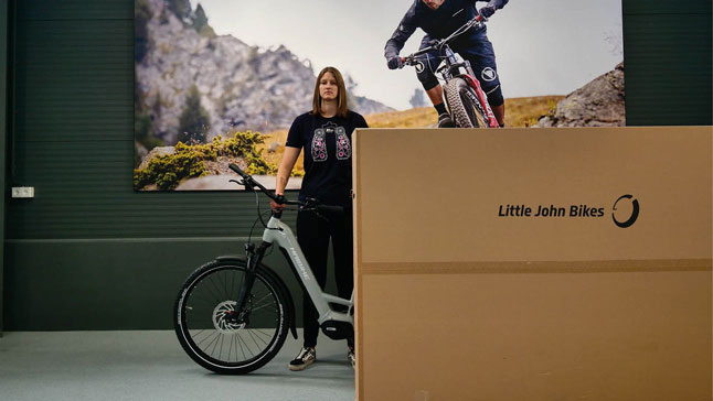 Eine Mitarbeiterin von Little John Bikes steht an einem Fahrradkarton.