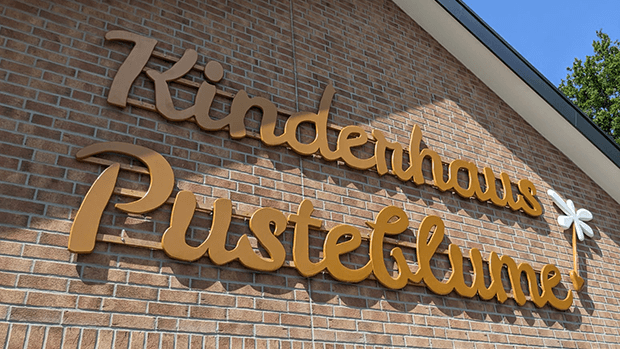 Schriftzug Kinderhaus Pusteblume an der Fassade des Gebäudes.