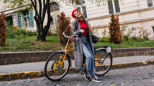 Junge Frau mit roter Mütze lehnt an einem gelben Fahrrad