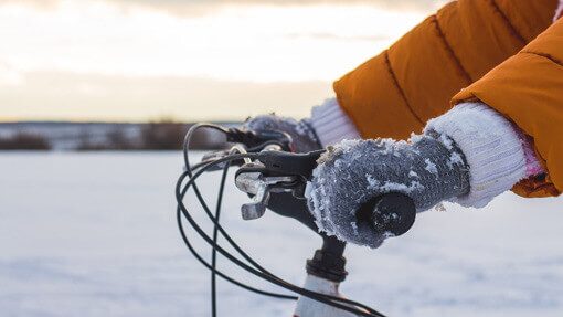 Hände in verschneiten Handschuhen halten Fahrradlenker