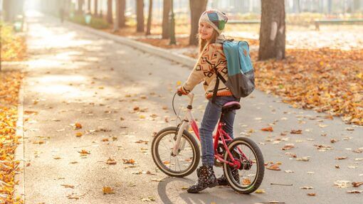 Ein Mädchen steht im Herbst mit rosa-weißem Fahrrad auf einem Weg und lacht