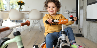 Kind fährt freudestrahlend auf seinem Dreirad durch das Zimmer