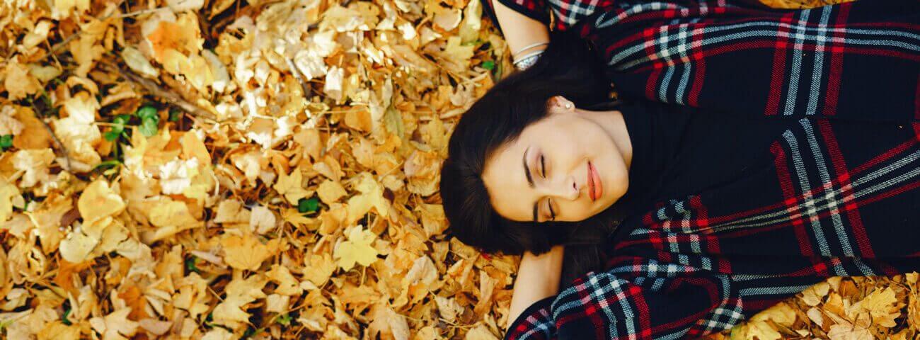 Eine junge Frau liegt mit geschlossenen Augen im Laub und lächelt