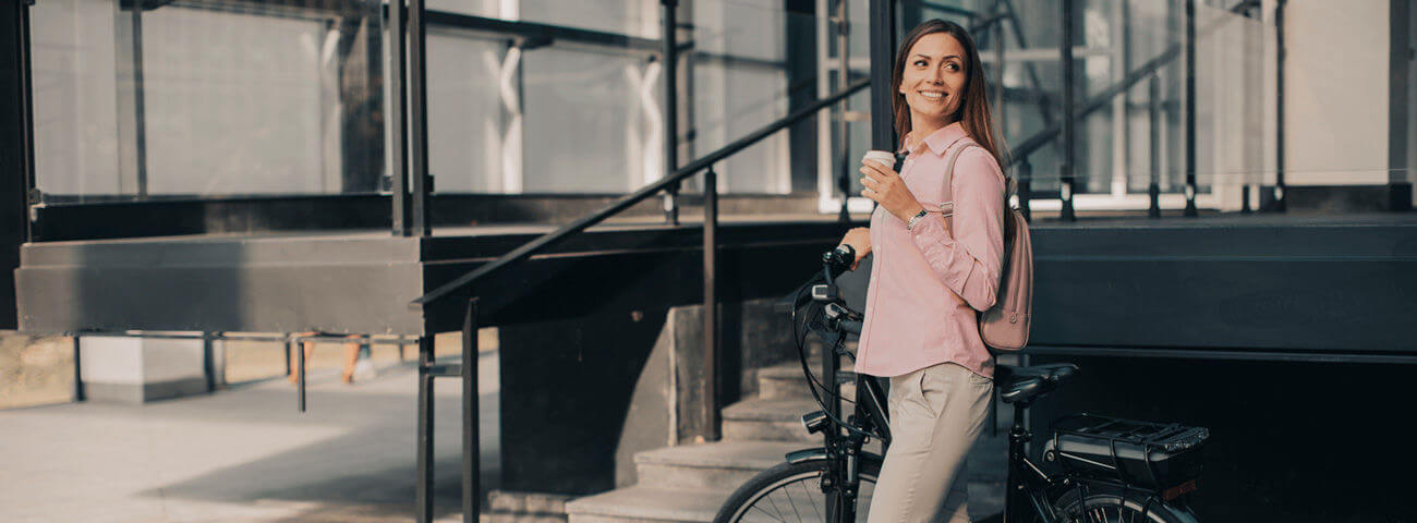 Junge Frau mit Fahrrad hält einen Kaffeebecher in der Hand