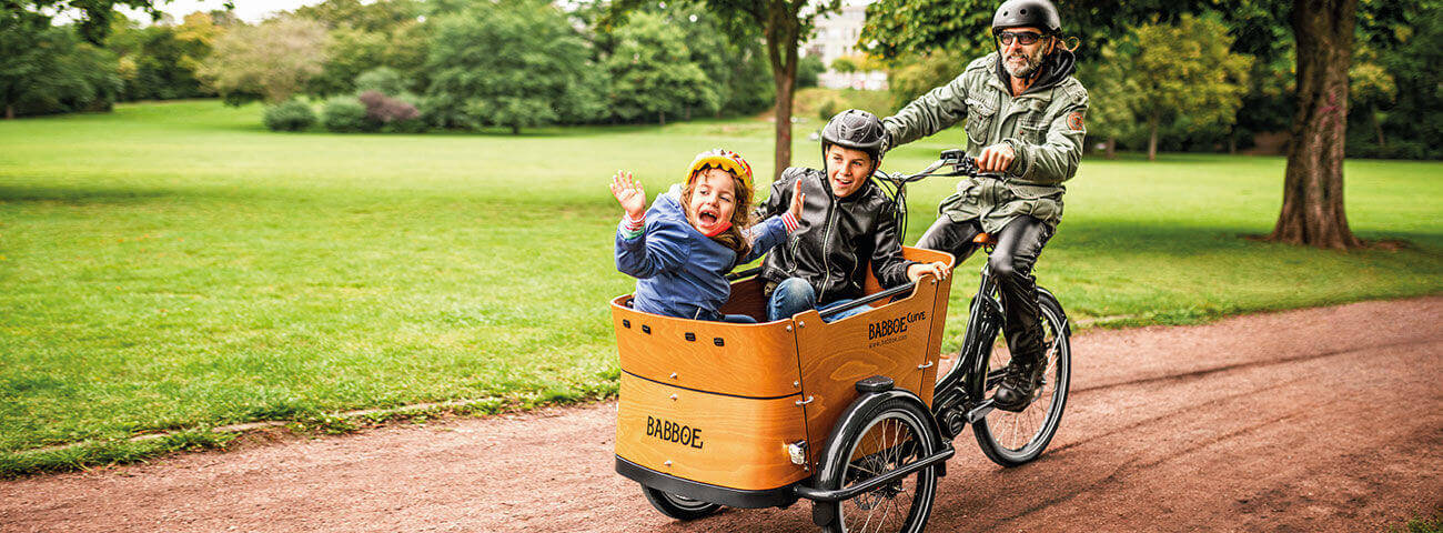 Rocker fährt auf Lastenrad Kinder durch einen Park