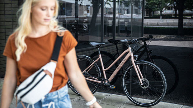 Blonde Frau mit Bauchtasche im Vordergrund läuft an einem Fahrrad vorbei