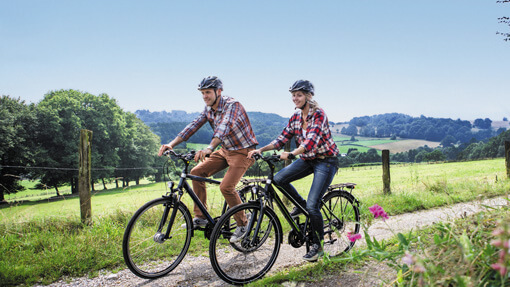 Zwei Radfahrer mit Helm fahren auf einem Weg durch eine grüne Landschaft